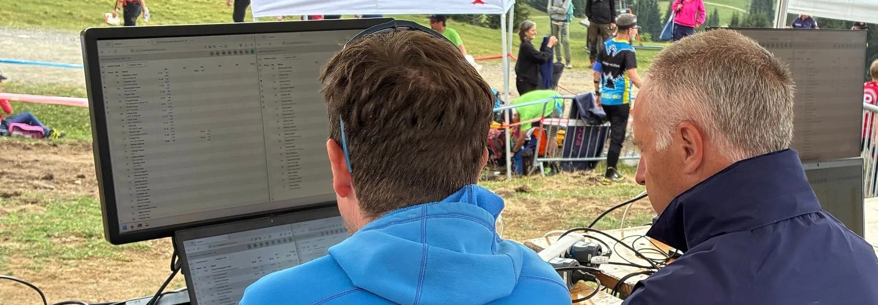 Zwei Männer sitzen vor einem Monitor auf dem Wettkampfergebnisse angezeigt werden. Wettkampfzentrale und Sprecher